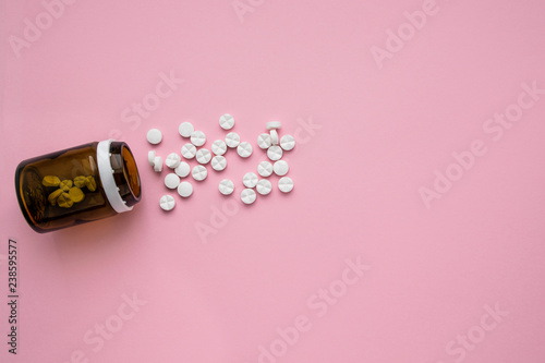 A bottle of medicines and scattered pills on a pastel pink background. Ripped vitamins on a bright background. Flat lay Top view photo
