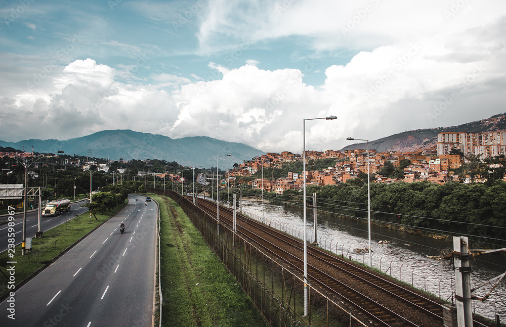 Highway, river and railway in the lush valley city of Medellín, Colombia, with the red houses of barrios built into the hills