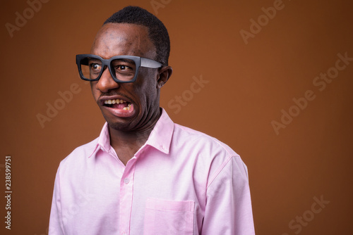 Portrait of young African businessman making faces against brown background © Ranta Images