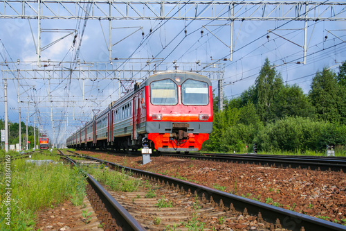 Red passenger electric train moves against the background of green trees