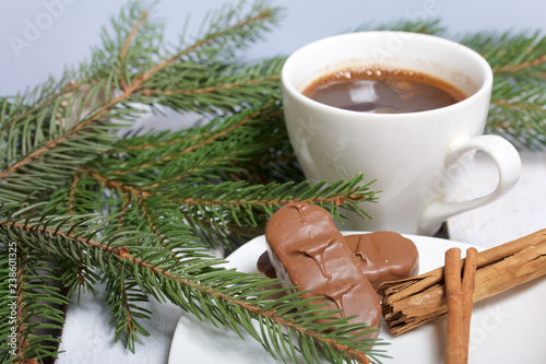 A cup of coffee, Cinnamon sticks and chocolate next to the fir branches. On a wooden box.