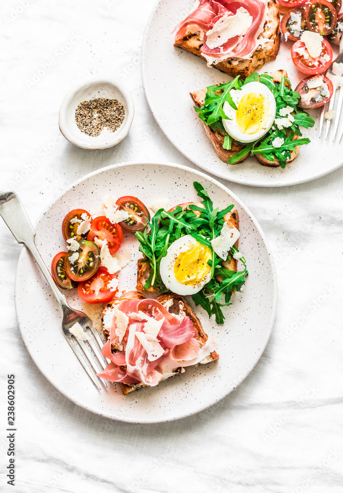 Delicious breakfast, snack, appetizers for wine, tapas - sandwiches with prosciutto, egg, arugula, cherry tomatoes and cream cheese on a light background, top view. Flat lay Delicious breakfast, snack, appetizers for wine, tapas - sandwiches with prosciutto, egg, arugula, cherry tomatoes and cream cheese on a light background, top view. Flat lay