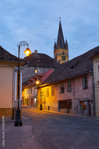 Twiight view of Typical cobbled stones street of city of Sibiu Romania, with colorful houses, church steeple and lampost photo