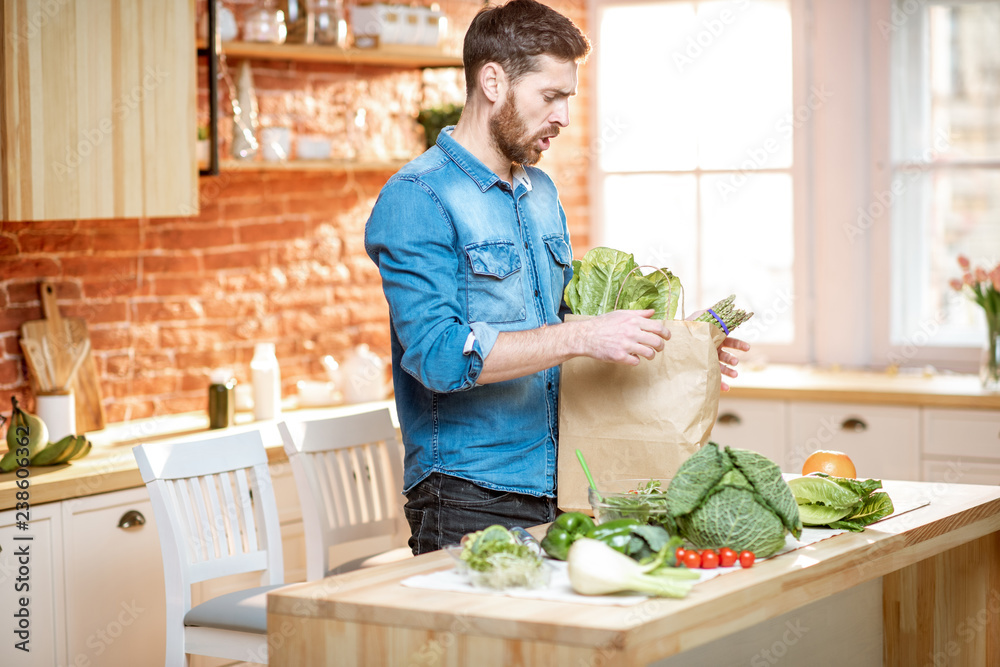 Handsome man in blue shirt unpacking healthy food from the shopping bag on the kitchen