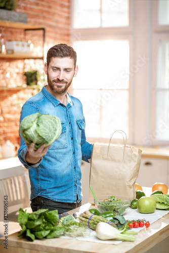 Handsome man in blue shirt unpacking healthy food from the shopping bag holding cabbage head on the kitchen