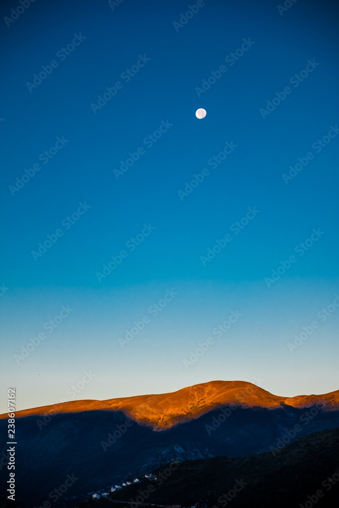 The moon setting as the sun rises over the Alps in France - sunlit peaks of mountains