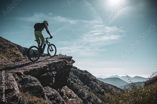 Obraz rowerzysta górski jedzie na dużą skałę głęboko w Alpach ze słońcem i górskimi warstwami