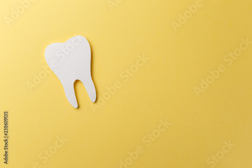 Photo White tooth on yellow background with copy space