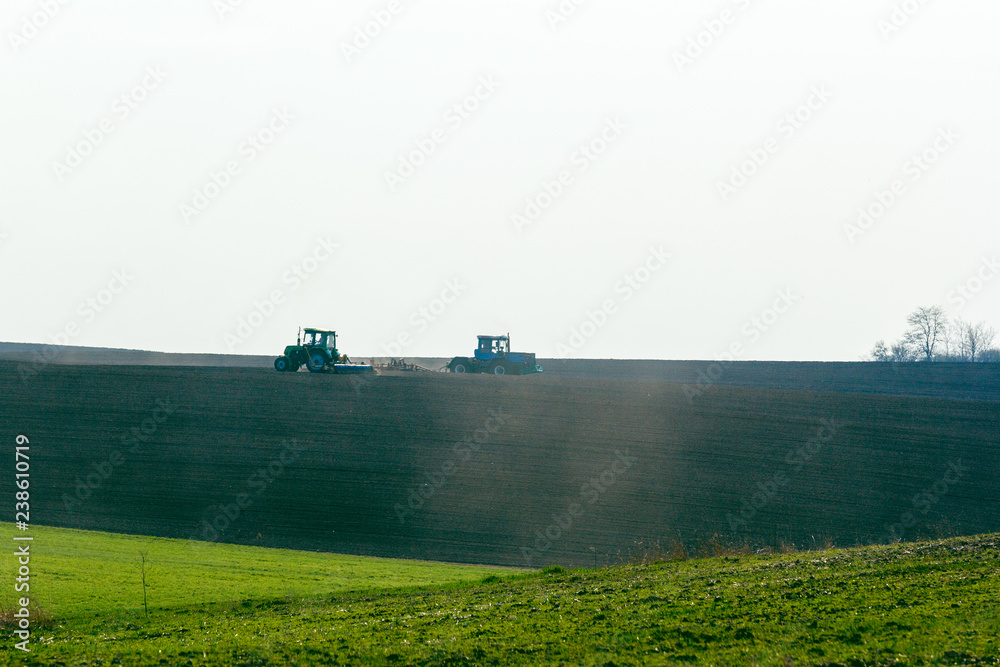 Naklejka premium Tractor cultivating field at spring
