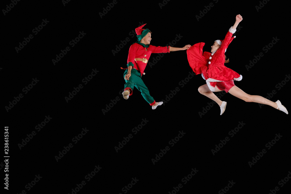 Christmas time, childhood, fairy tale. A young girl wearing a Santa's costume and boy wearing elf costume flying together