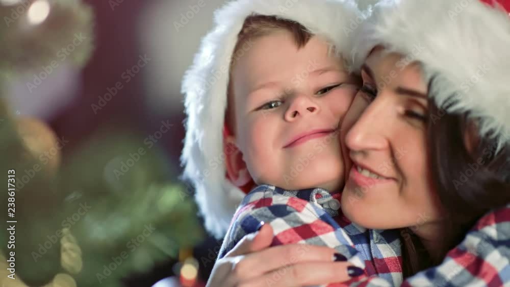 Happy family mother and cute little son hugging and smiling together near Christmas tree close-up Happy family mother and cute little son hugging and smiling together near Christmas tree close-up