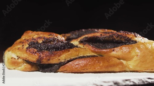 Swirl bun with poppy seeds falls on the table with flour, slow motion. Poppy seed braided or roll bread on slate. photo