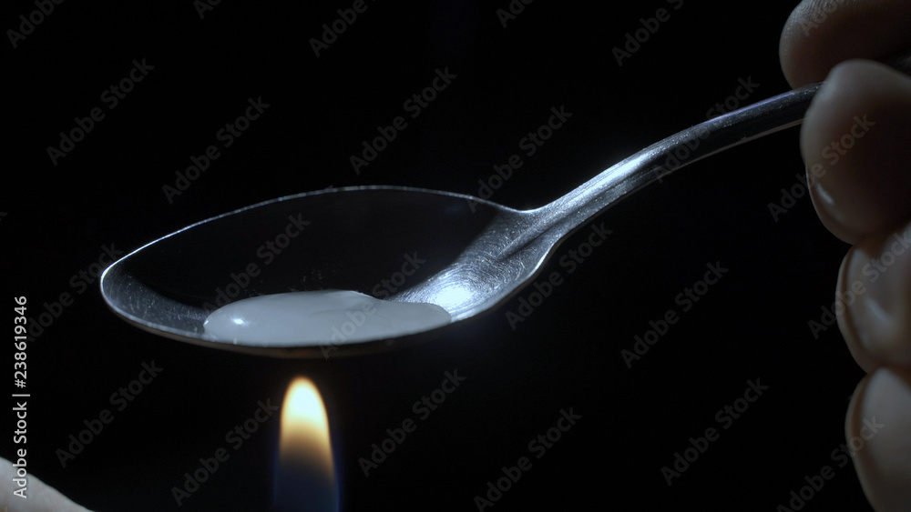 addict heating heroin in a spoon over a flame addict heating heroin in a spoon over a flame