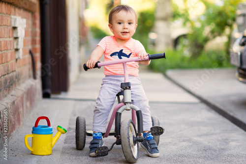 Tableau sur toile Portrait of a little child on a three wheel bike (tricycle) on a tarmac pavement in a warm sunny day