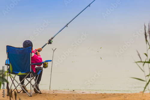 Boy Sitting on a Chair at the Riverside and Looking at the fishing rod, Catching Fish Using his Fishing Rod