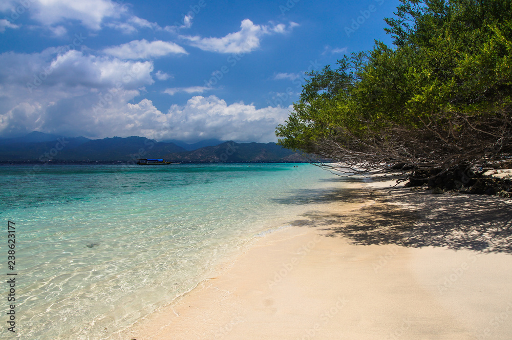 Sandy beach with blue water on the tropical island of Gili Meno. The mountains of Lombok on the horizon.