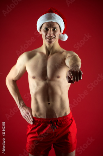 Sexy athletic macho in santa claus hat. If you were very bad girl. Macho sexy muscular torso posing confidently. Santa claus comes not only to good girls. Athlete man wear santa hat and red shorts © be free