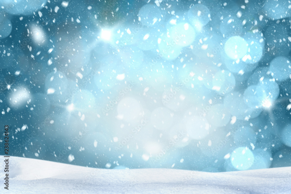 Fototapeta premium Falling snow with white snow on the ground at night and freezing blue tone bokeh of lights in background. Copy space.