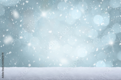 Falling snow with white snow on the ground and freezing blue tone bokeh of lights in background. Copy space.