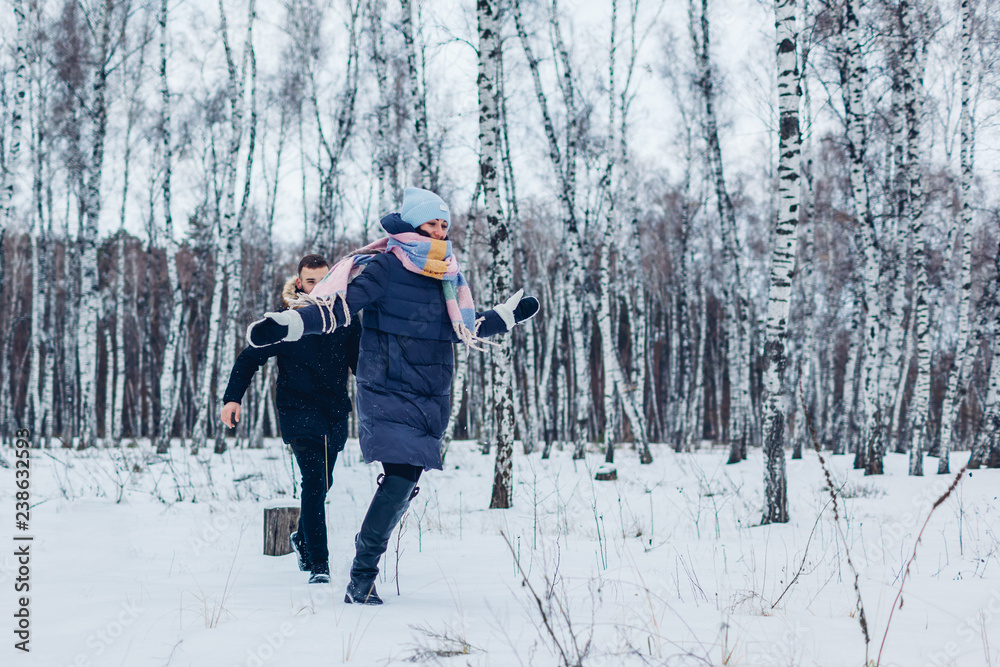 Beautiful loving couple running in winter forest together. People having fun outdoors