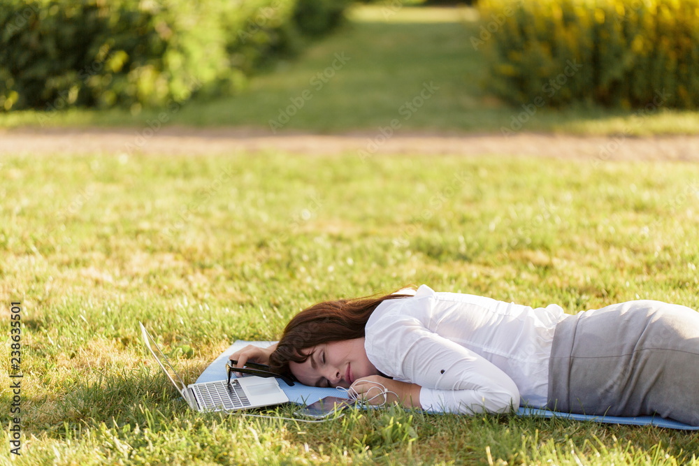 Business woman lying on a green grass and sleeping next to her laptop. Business woman lying on a green grass and sleeping next to her laptop.