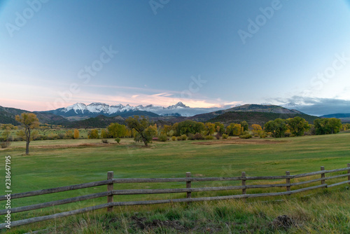 A distant snow capped mountain range in front of rolling green farm land