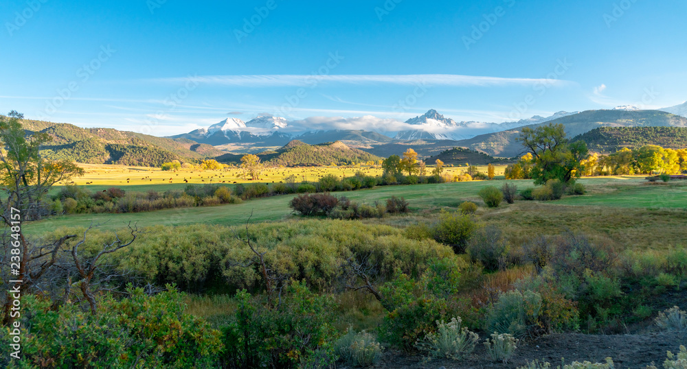Obraz premium The sun is about to set over a ranch in the colorado mountains filled with cows and surrounded by fences