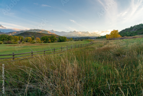 The sun is about to set over a ranch in the colorado mountains filled with cows and surrounded by fences