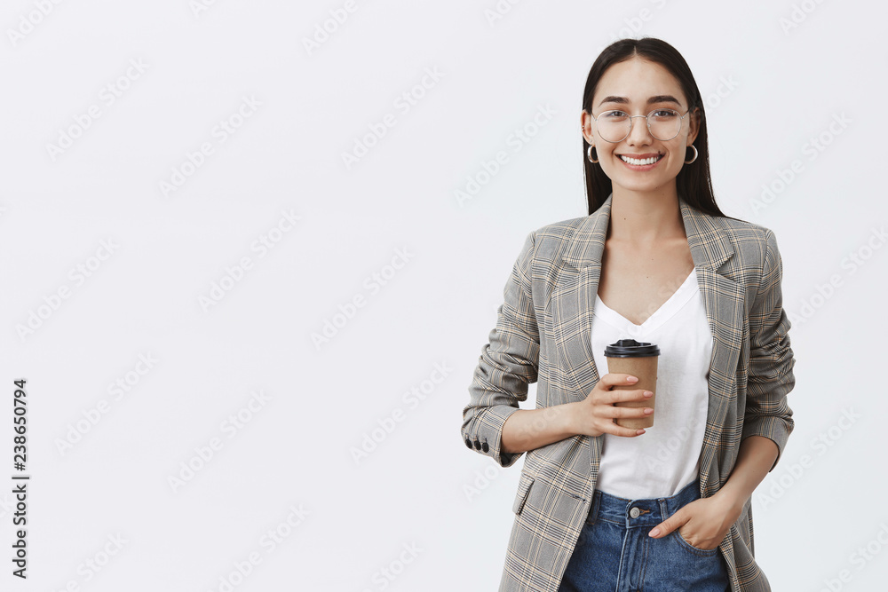 Wanna grab coffee. Portrait of relaxed and confident european woman with dark hair and glasses, holding hand in pocket and drinking tea in local cafe, enjoying great working day over gray background Wanna grab coffee. Portrait of relaxed and confident european woman with dark hair and glasses, holding hand in pocket and drinking tea in local cafe, enjoying great working day over gray background