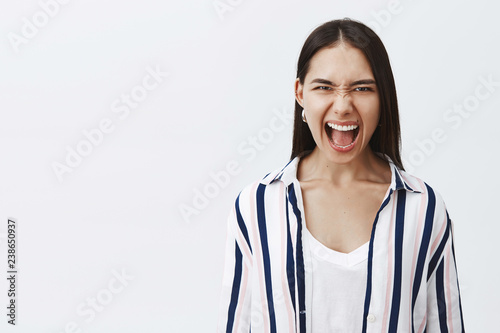 Woman in middle of fight, shouting at ex-boyfriend who cheated on her. Portrait of angry sick and tired female in striped blouse, wrinkling nose and frowning while yelling at camera with anger photo