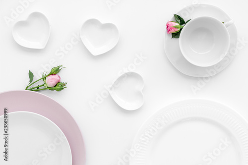 Simple color table setting for celebration with roses, pink plates and heart-shaped saucers on white table background top view