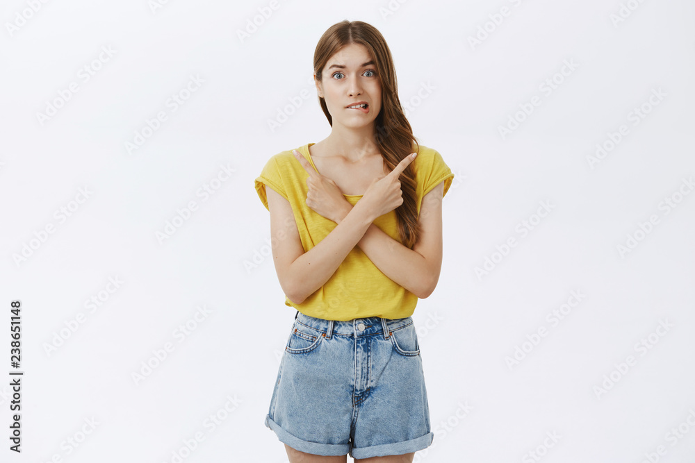 Hesitant girl worries to make choice pointing right and left in different corners of copy space biting lip anxiously making important decision being clueless what right or wrong over gray background Hesitant girl worries to make choice pointing right and left in different corners of copy space biting lip anxiously making important decision being clueless what right or wrong over gray background