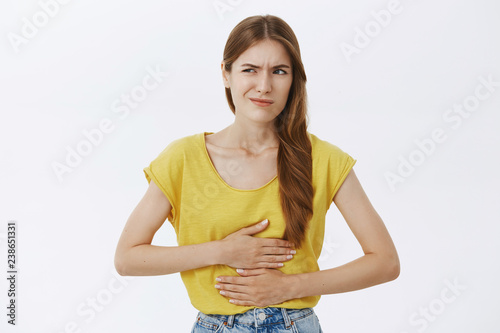 Girl regret eating food near subway. Portrait of displeased worried woman feeling discomfort in stomach holding hands on belly smirking and frowning looking left having stomachache or disorder photo