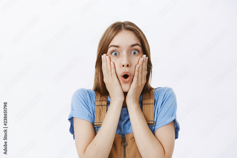 Waist-up shot of amazed and surprised good-looking impressed woman gasping opening mouth and folding lips in excitement pressing hands to cheeks from amazement standing shocked over gray background Waist-up shot of amazed and surprised good-looking impressed woman gasping opening mouth and folding lips in excitement pressing hands to cheeks from amazement standing shocked over gray background