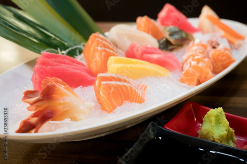 Mixed sliced fish sashimi on ice in white bowl. Sashimi Salmon Tuna Hamachi Prawn and Surf Calm set, raw fish, japanese food in Asian restuarant.