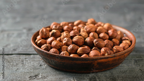 A clay bowl full of walnut kernels on a black rustic table. Vegetarian cuisine.