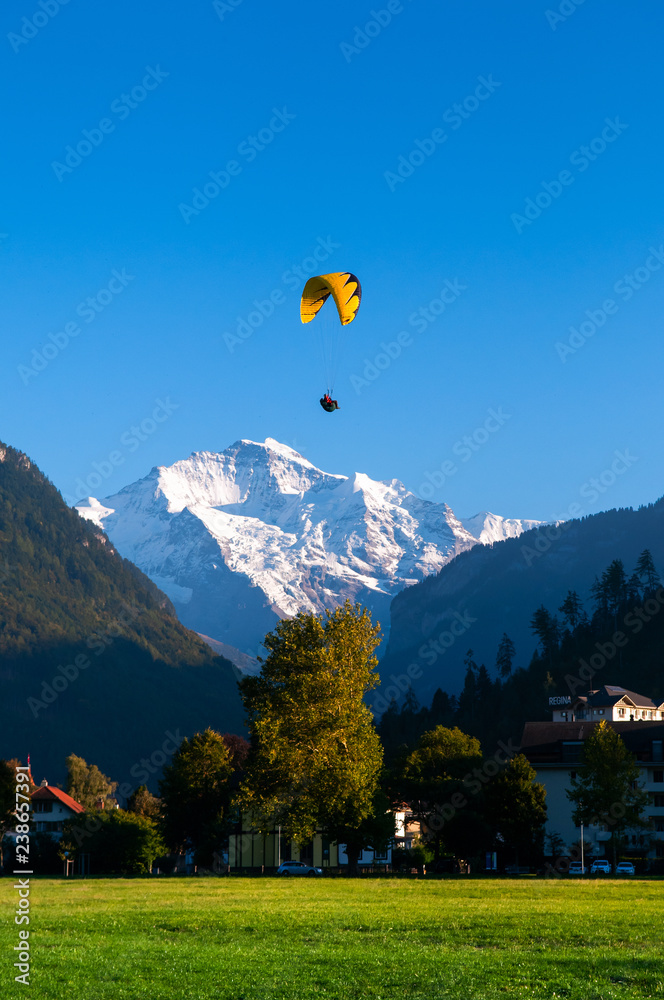 Paragliding flying over green field Hohematte park and Swiss alps in  Interlaken, Switzerland Photos | Adobe Stock