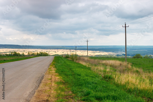 The asphalt rural road leading to the sandy wilderness at the distance © Alexey Slyusarenko
