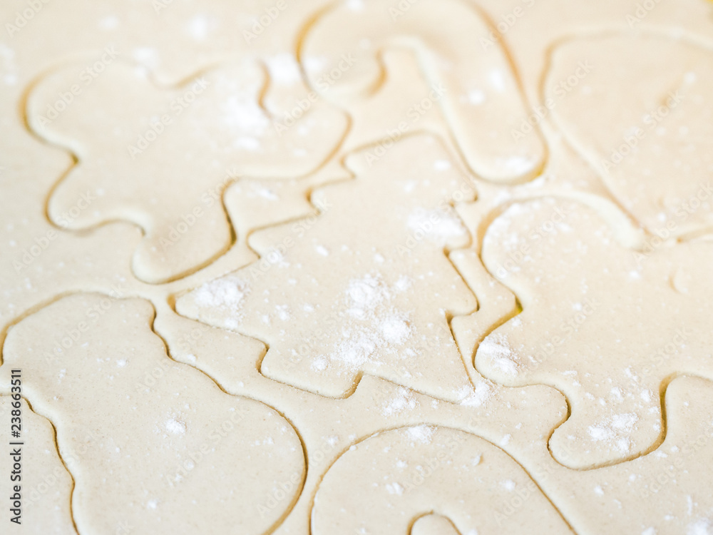 A closeup of a Christmas tree cutout and other holiday stencils or shapes including gingerbread man cut in raw sugar cookie dough with flour sprinkled on top making a beautiful festive background. A closeup of a Christmas tree cutout and other holiday stencils or shapes including gingerbread man cut in raw sugar cookie dough with flour sprinkled on top making a beautiful festive background.