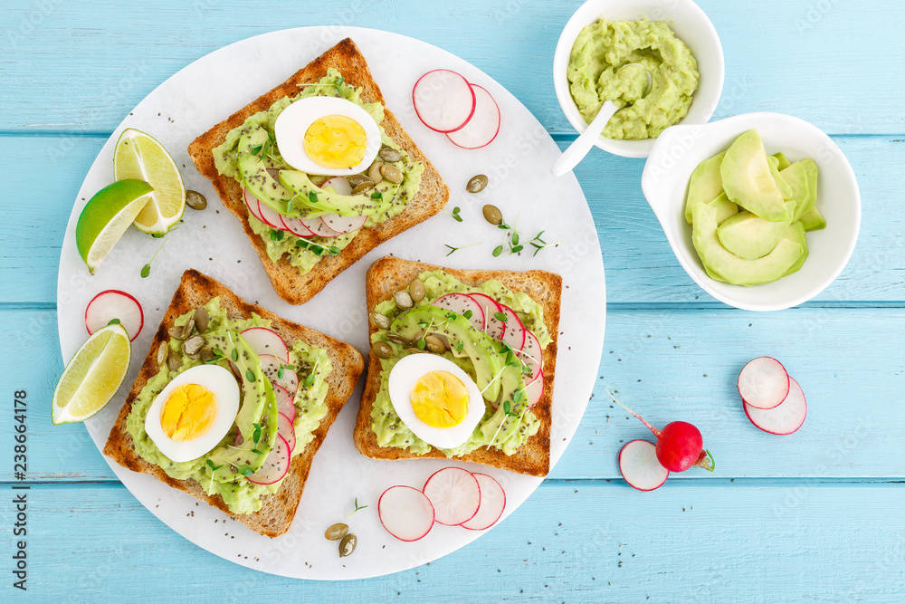 Toasts with avocado guacamole, fresh radish, boiled egg, chia and pumpkin seeds. Diet breakfast. Delicious and healthy plant-based food. Flat lay. Top view Toasts with avocado guacamole, fresh radish, boiled egg, chia and pumpkin seeds. Diet breakfast. Delicious and healthy plant-based food. Flat lay. Top view
