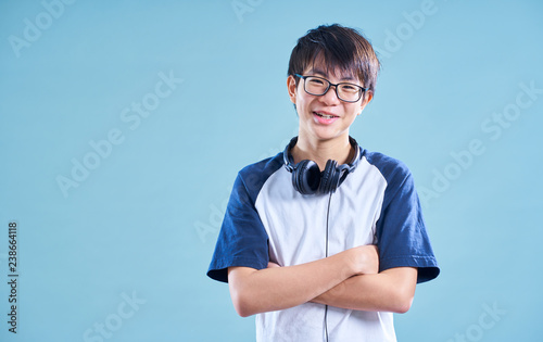Portrait of Asian teenage smiling boy in studio with light blue background . Music headphone concept .