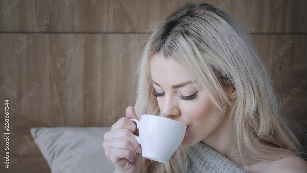 Beautiful blonde woman holding ceramic cup of tea or coffee enjoy. Tea time in bed room. Looking at window and drink tea. Good morning. Pretty young girl relaxing. Happy winter concept. Beautiful blonde woman holding ceramic cup of tea or coffee enjoy. Tea time in bed room. Looking at window and drink tea. Good morning. Pretty young girl relaxing. Happy winter concept.