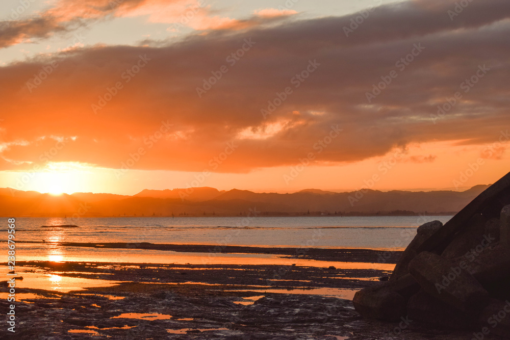 A pale orange sun sets above the calm beach in Gisborne, New Zealand.