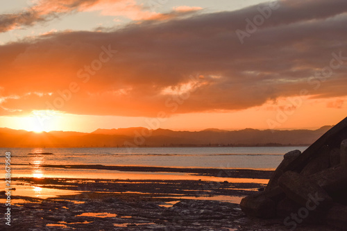 A pale orange sun sets above the calm beach in Gisborne  New Zealand.