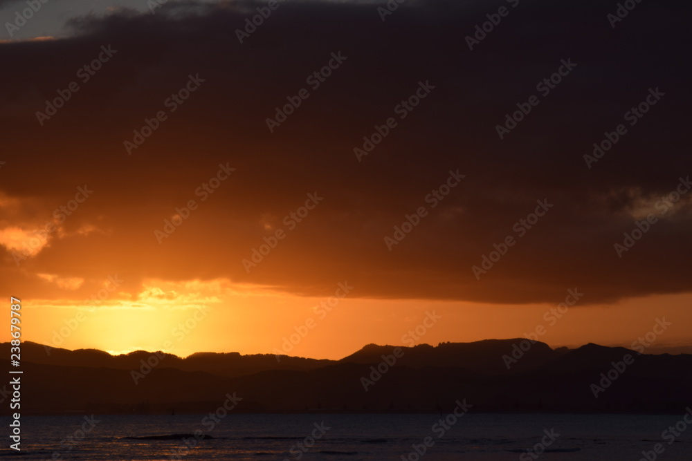 A dark hill l;andscape below the sinking orange sunset at Gisborne, New Zealand.