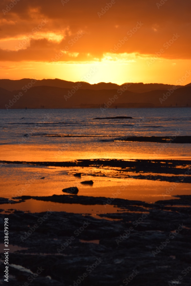 A orange sun sets above the hills reflected in the sea water at Gisborne, New Zealand.