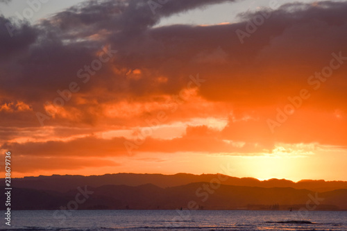 A coral colored sky while the sun sets above the beach in Gisborne, New Zealand.