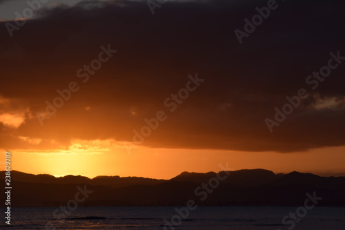 A dark hill l;andscape below the sinking orange sunset at Gisborne, New Zealand.