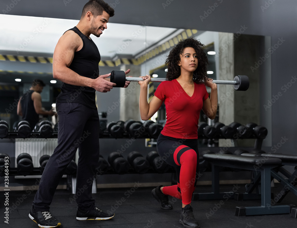 Personal instructor helping woman with barbell squats Personal instructor helping woman with barbell squats