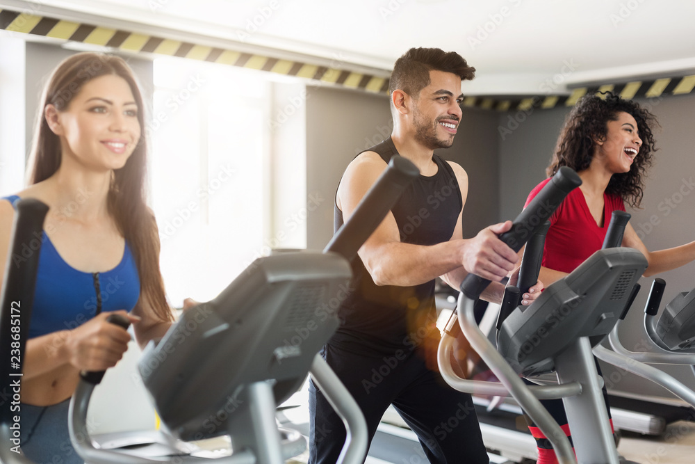 Young people exercising on cross-trainer in gym Young people exercising on cross-trainer in gym